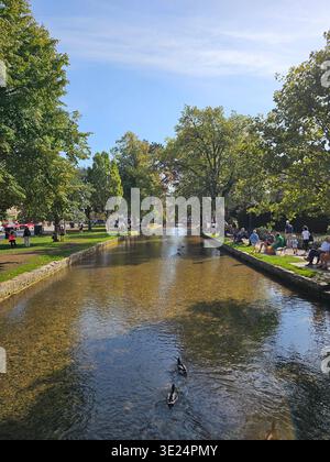 Ein geschäftiger Sommertag in Bourton-on-the-Water zeigt Besuchern, wie sie sich am Fluss entspannen, der von einer Brücke im Herzen der Cotswolds gefangen wird. Stockfoto