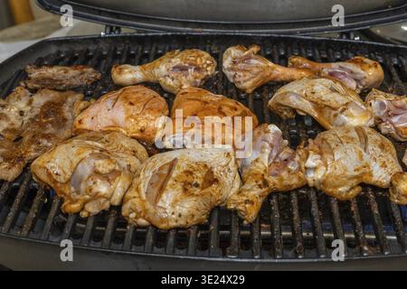 Verschiedene Stücke von rohem Huhn und Schweinefleisch, mit Gewürzen gewürzt, werden auf einem schwarzen Metallgitter mit sichtbarer Hitze angeordnet Stockfoto