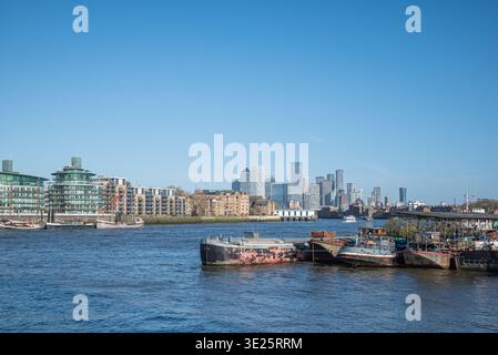 Blick über die Themse auf Boote im Vordergrund und die Skyline von Canary Wharf in der Ferne. London, Großbritannien. Stockfoto