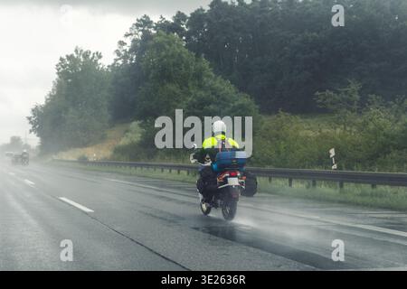 Motorradfahrer fahren auf nasser Autobahn im Regenschauer mit geringer Sicht umgeben von grünem Waldnebel. Die reflektierende Jacke für Tourenreiter reist stürmisch Stockfoto