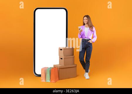Eine junge Frau hält ihr Smartphone, während sie neben einer großen Umrisse eines Telefons steht Stockfoto