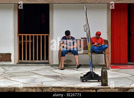 PIRENÓPOLIS, Goiás, BRASILIEN - 15. Januar 2026: Zwei junge Männer auf ihren Handys vor einer kolonialen Gebäudefassade Stockfoto