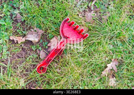 Ein roter Spielzeugarchen aus Plastik liegt auf grünem Gras mit Bodenflecken und trockenen braunen Blättern, die in der Nähe im Freien verstreut sind. Stockfoto
