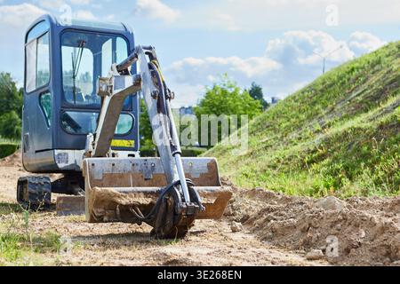 Der Mini-Raupenbagger gräbt den Boden an einem sonnigen Tag Stockfoto