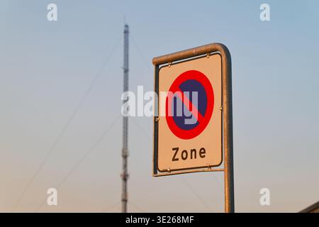 Ein Verkehrsschild, das auf einem Metallmast montiert ist, mit einem Kommunikationsturm und klarem Himmel im Hintergrund während der Tageslichtstunden. Stockfoto