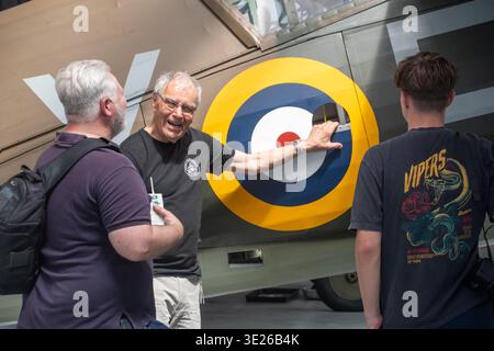 IWM Duxford Summer Airshow - ein älterer Reiseleiter zeigt animiert auf einen großen RAF-Rounddel in einem restaurierten Militärflugzeug, während zwei Besucher in einer avia lauschen Stockfoto