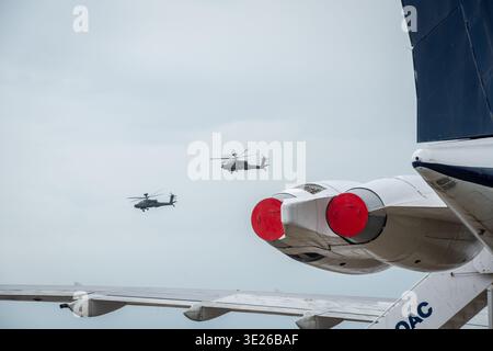 IWM Duxford Summer Airshow - Militärhubschrauber fliegen in enger Formation neben dem Flügel und den Motoren eines geparkten Jets an einem Küstenflughafen, was an AVI erinnert Stockfoto