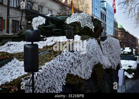 Seitenansicht eines getarnten Panzerpanzers mit langem Kanonenlauf und weißem Tarnnetz, der während einer öffentlichen Militärausrüstung auf einer Stadtstraße steht Stockfoto