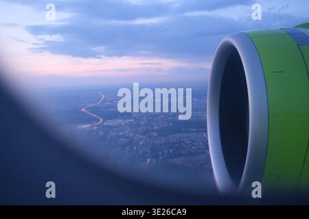 Flugzeugtriebwerk über der beleuchteten Stadt in der Dämmerung, aus der Vogelperspektive vom Beifahrersitz aus Stockfoto
