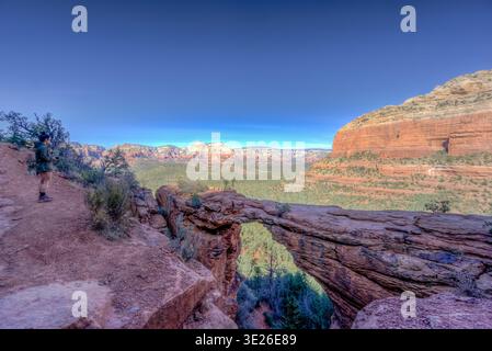 Ein Mann steht auf einer Brücke und blickt über einen Canyon. Der Himmel ist klar und die Sonne scheint hell. Die Brücke besteht aus Stein und der Canyon Stockfoto