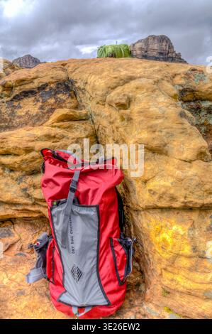 Ein roter Rucksack sitzt auf einem felsigen Hügel. Der Rucksack wurde von Columbia hergestellt und ist für Rucksacktouren konzipiert. Das Bild hat ein stimmungsvolles und abenteuerliches Gefühl Stockfoto