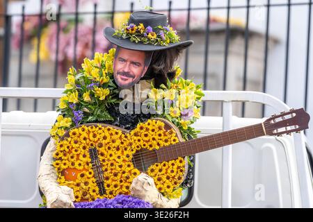 Festival de Flores - Antigua Guatemala - Ein kostümierter Künstler mit einer geblümten Gitarre und Papiermaske trägt einen Hut und einen Kranz aus gelben und lila Blumen Stockfoto