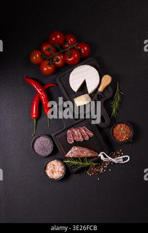 Gourmet-Aufschnitt, frischer Käse, rote Chili-Paprika, reife Kirschtomaten und verschiedene Gewürze auf dunklen Holzbrettern schaffen ein elegantes Ambiente Stockfoto