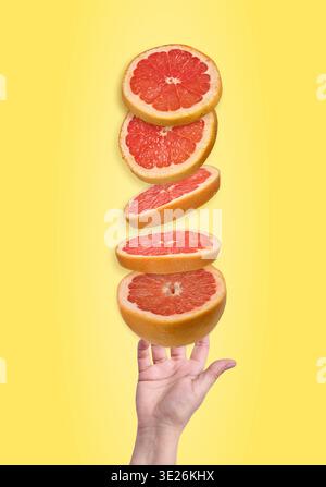 Fünf saftige rote Grapefruitscheiben schweben in der Luft über einer offenen Palme vor einem hellgelben Hintergrund. Stockfoto