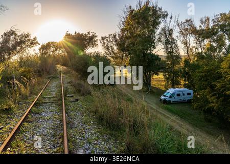 Eindrucksvolle wilde Campingszene in Sizilien. Ein weißer Wohnmobil befindet sich im Belice Reservat, das neben alten Bahngleisen als goldenes Licht bei Sonnenuntergang parkt Stockfoto