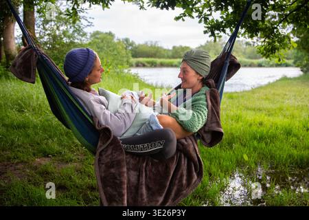 Zwei Frauen entspannen sich in einer Hängematte an der Themse in Oxfordshire und genießen Unterhaltung und Natur Stockfoto