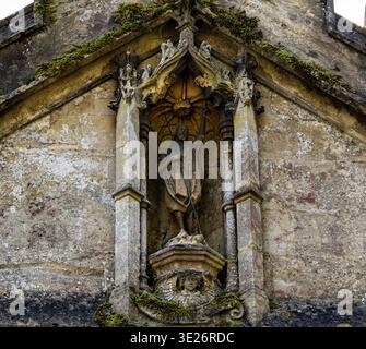 Steinstatue eines heiligen mit einem Kreuz in einer reich verzierten gotischen Architekturnische an einer alten verwitterten Kirchenfassade St. John the Baptist Pewsey Wilts Stockfoto