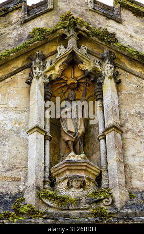 Antike Steinstatue eines heiligen in einer gotischen Steinnische an der verwitterten Fassade einer historischen Kirche mit Moos und architektonischen Details Stockfoto