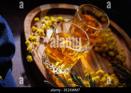 Zwei Gläser Amber Whiskey auf Holztablett mit Mimosa Flowers Luxury Drink Stillleben Stockfoto