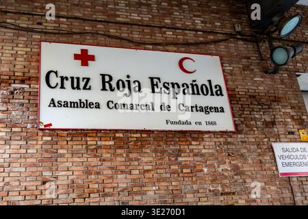 Hauptquartier des spanischen Roten Kreuzes in Cartagena, Spanien, mit einer Ziegelfassade mit Beschilderung für die lokale Versammlung und einem Notfahrzeug-Ausstiegsschild. Stockfoto