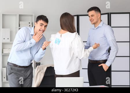 Junge Männer und ihre Kollegin mit klebrigem Papier im Büro. Aprilfeier Stockfoto
