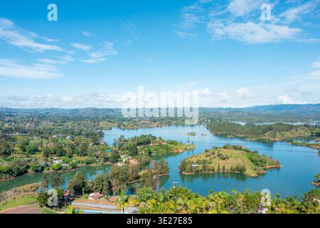 Panorama des Guatapé-Stausees mit smaragdgrünem Wasser, verstreuten Inseln, baumbewachsenen Hügeln und Häusern unter klarem blauen Himmel – malerische tropische Landschaft in Stockfoto