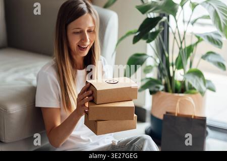 Junge kaukasische Frau, die Papier Öko-Tasche zum Mitnehmen auspackt, als Kurierdienst für Lebensmittel zu Hause in einer modernen Wohnung Stockfoto