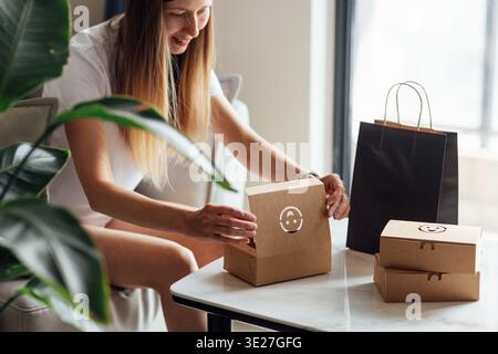 Junge kaukasische Frau, die Papier Öko-Tasche zum Mitnehmen auspackt, als Kurierdienst für Lebensmittel zu Hause in einer modernen Wohnung Stockfoto