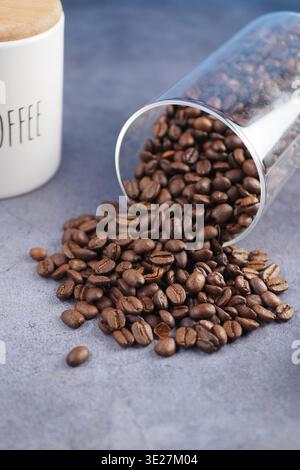 Kaffeebohnen, die aus einem Glasbehälter auf dem Tisch verschüttet werden Stockfoto