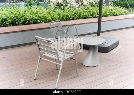 Sitzplätze im Freien mit Metallstühlen und rundem Tisch auf Holzterrasse in der Nähe von Grün in Singapur Stockfoto