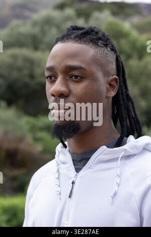 Afroamerikaner, der links schaut, trägt einen weißen Hoodie mit Reißverschluss, Streicher und ein dunkles Hemd im Park Stockfoto