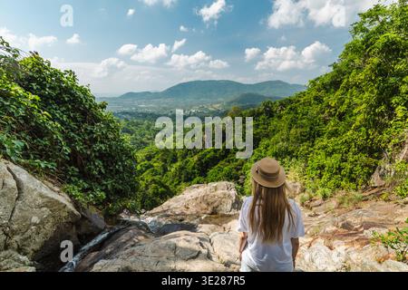 Junge Frau, die auf einem felsigen Felsvorsprung mit Blick auf das tropische Tal und die fernen Hügel steht, friedliche Sommerreise in einer üppig grünen Waldlandschaft Stockfoto