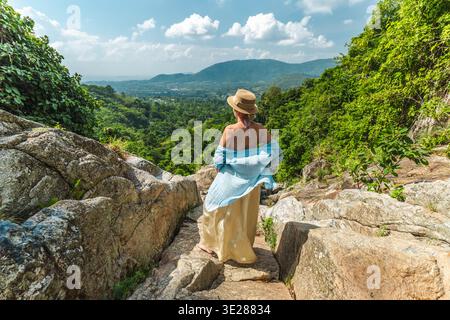 Junge Frau, die am felsigen Aussichtspunkt des Wasserfalls mit Blick auf das üppige tropische Tal und die Berge auf Koh Samui Thailand steht Stockfoto