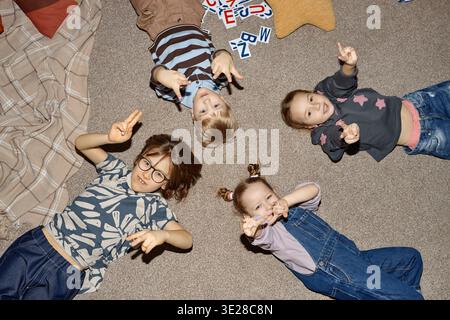 Gruppe multiethnischer Kinder, die auf dem Boden liegen und mit den Fingern im Kindergarten zeigen Stockfoto