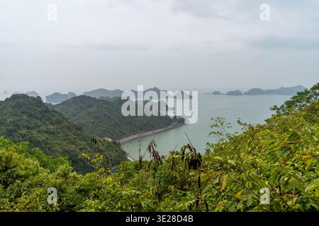 Ein malerischer Blick auf die üppigen grünen Berge, die auf das ruhige Meer treffen, mit Inseln am Horizont unter einem bewölkten Himmel Stockfoto
