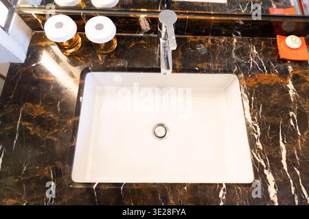 Weißes rechteckiges Waschbecken auf schwarzer Marmorarbeitsfläche mit Chromarmatur in modernem Bad, Top-down Stockfoto