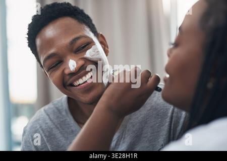 Glückliches, Hautpflege und schwarzes Paar zu Hause mit Gesichtsmaske für gesunde Haut, Wellness und Bindung. Ehe, verspielt und Mann mit Frau mit Gesicht Stockfoto