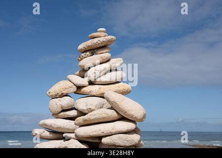 Zen gestapelte Steine balancieren auf einem Strand mit blauem Himmel und Ozean Horizont Hintergrund Stockfoto