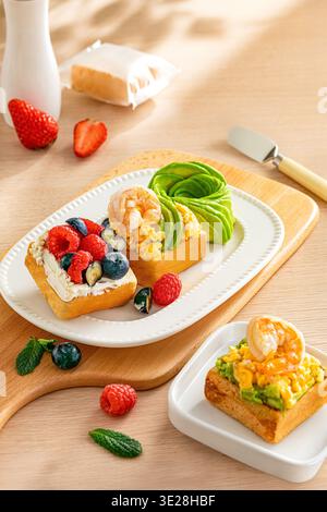 Offene Gourmet-Sandwiches mit Avocado-Garnelen-Rührei und gemischten Beeren auf Holzbrett Stockfoto
