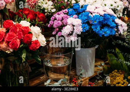 Verschiedene Blumensträuße mit Rosen und Chrysanthemen stehen in Vasen auf hölzernem Display. Muttertagsgeschenke, nachhaltige Blumen, umweltfreundliche Verpackungen. Stockfoto