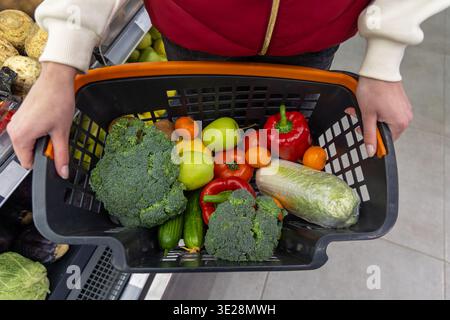 Warenkorb mit frischem Obst und Gemüse. Draufsicht eines Käufers, der einen Korb mit frischem Gemüse und Obst in einem Lebensmittelgeschäft hält Stockfoto