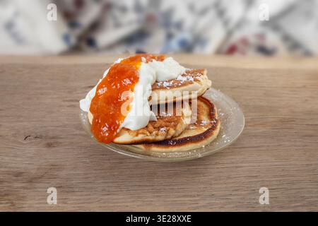 Pfannkuchen mit Puderzucker, griechischem Joghurt und Pfirsichmarmelade auf Holztisch, Seitenansicht Stockfoto