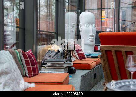 Moderne Lounge mit orangefarbener Bank, weißen Kopfskulpturen und Stadtfenstern Stockfoto