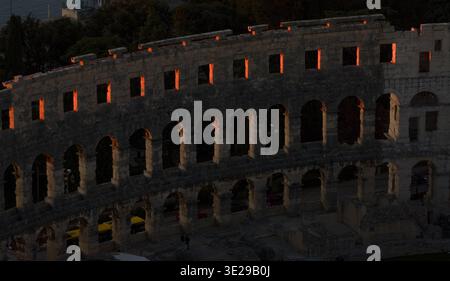 Aus der Vogelperspektive des antiken römischen Amphitheaters, das in das warme Licht der untergehenden Sonne getaucht ist und lange Schatten auf seiner verwitterten Steinfassade, Pula, I, wirft Stockfoto