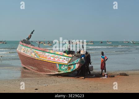 Eine kleine Gruppe von Fischern auf der Rückseite eines hölzernen Fischerbootes (Pirogue) am Strand von Kafountine bei Ebbe. Senegal Stockfoto