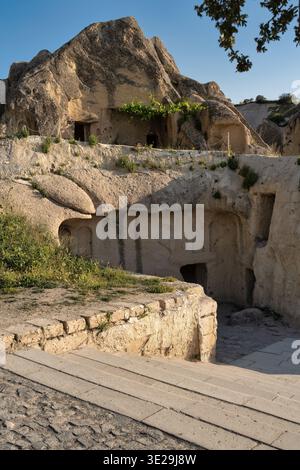 Steintreppen führen zu alten Höhlenhäusern, die in einzigartige Felsformationen in Goreme, Kappadokien, Türkei, unter einem klaren blauen Himmel gemeißelt wurden. Historische Architektur Stockfoto