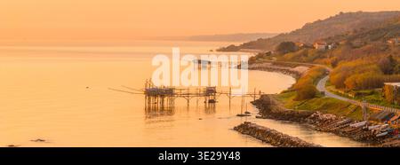 Aus der Vogelperspektive das goldene Licht, das die Küste von Trabocchi taucht, wo alte Fischplattformen auf die gewundene Küstenstraße treffen, San Vito Chietino, Abruzzen, IT Stockfoto