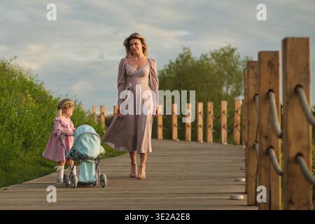 Bei einem Spaziergang auf einer Holzbrücke genießen Mutter und Tochter einen Abendspaziergang. Die Szene spiegelt den Alltag der Familie wider. Stockfoto
