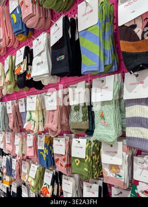 Bunte Socken hängen ordentlich auf einem pinkfarbenen Präsentationsständer. Jedes Paar hat ein Etikett und ein einzigartiges Muster oder Design. Zu den sanften Farbtönen gehören Rosa, Grün, Blau und Violett Stockfoto