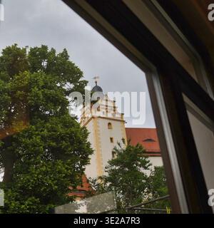 Gerahmter Blick aus einem Fenster auf den markanten Schlossturm von Schloss Colditz hinter grünen Bäumen im Landkreis Leipzig Stockfoto